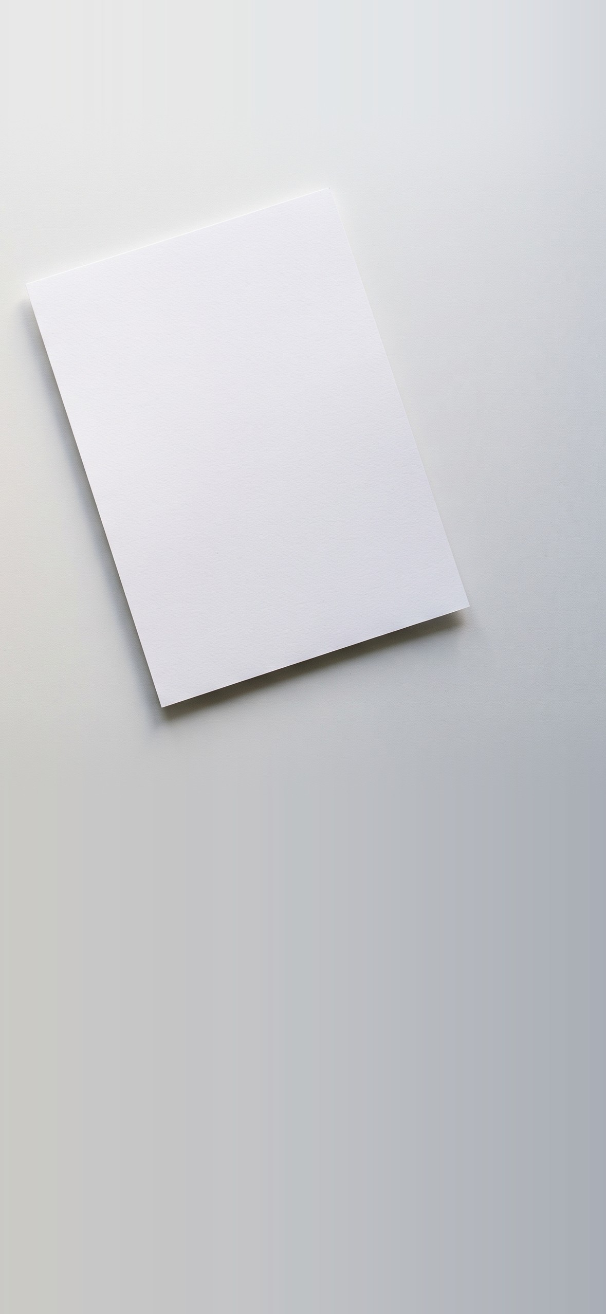 A white sheet of paper on an otherwise empty, light gray desk, photographed from above.