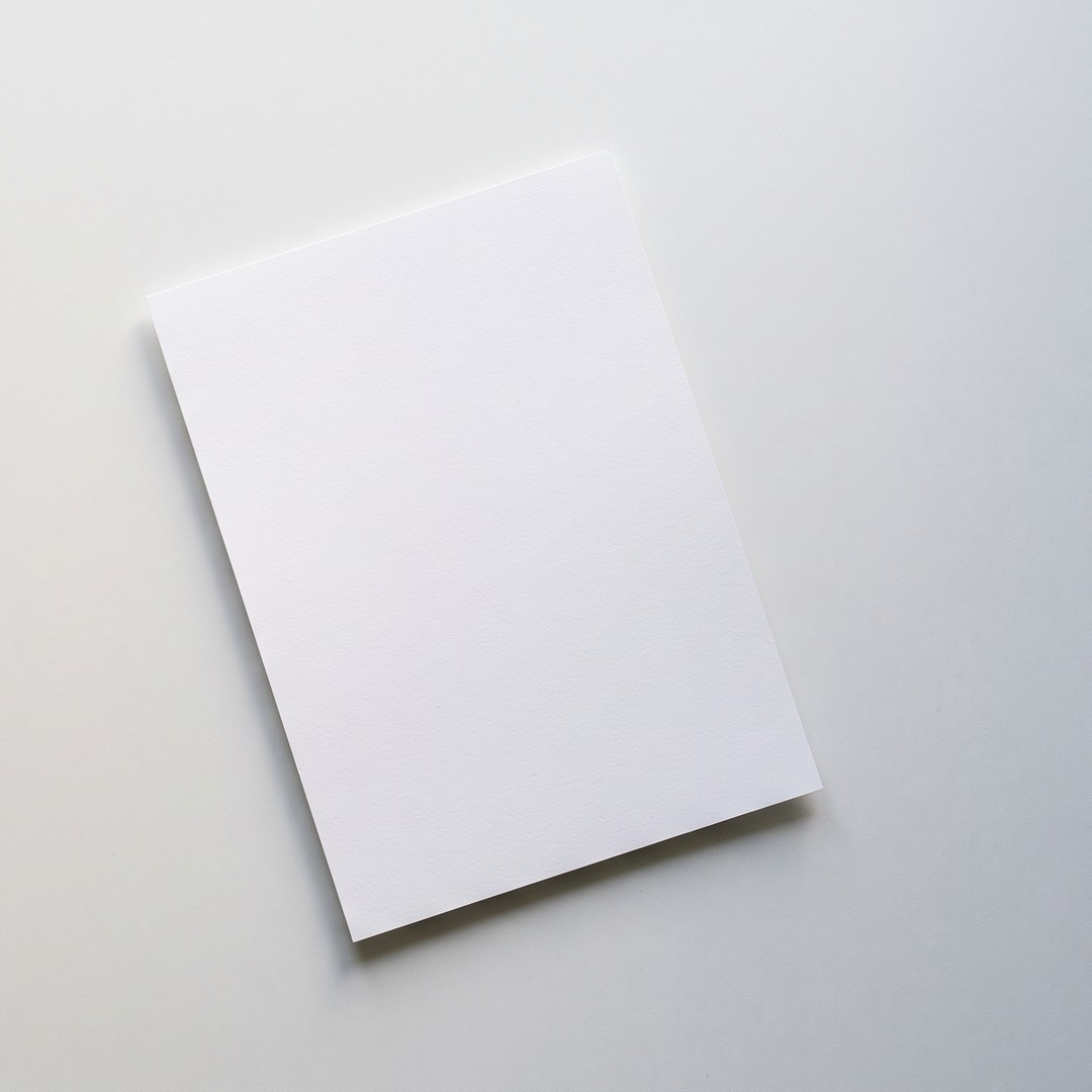 A white sheet of paper on an otherwise empty, light gray desk, photographed from above.